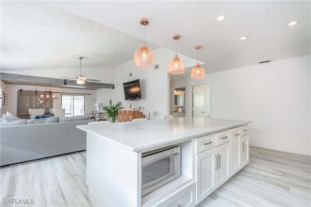 kitchen with vaulted ceiling, a barn door, white cabinetry, ceiling fan, and stainless steel microwave