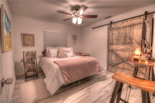 bedroom featuring a barn door, ceiling fan, and light wood-type flooring