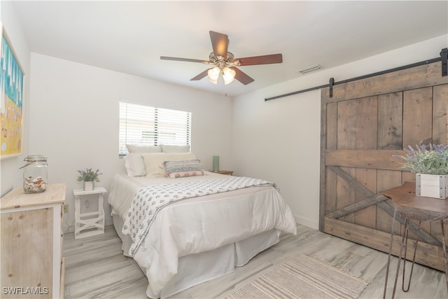 bedroom with light hardwood / wood-style flooring, ceiling fan, and a barn door