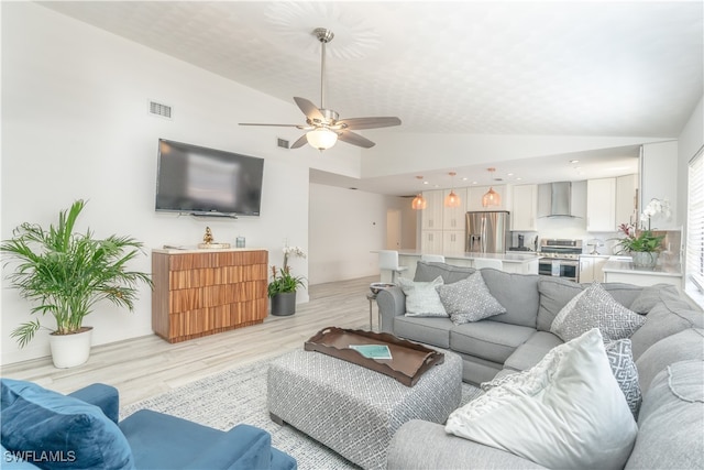 living room with ceiling fan, light hardwood / wood-style floors, and vaulted ceiling