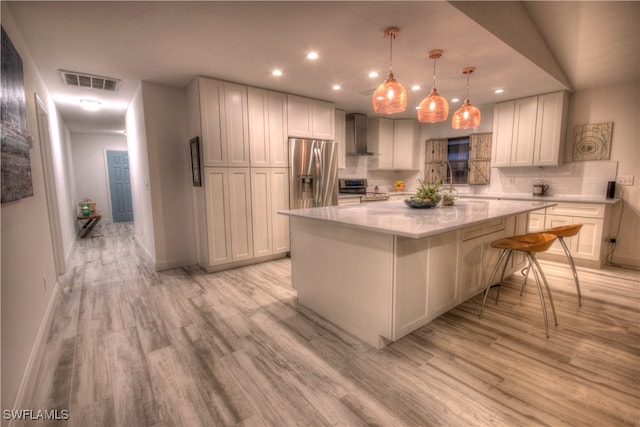 kitchen with a kitchen island, light hardwood / wood-style floors, stainless steel appliances, white cabinetry, and wall chimney range hood