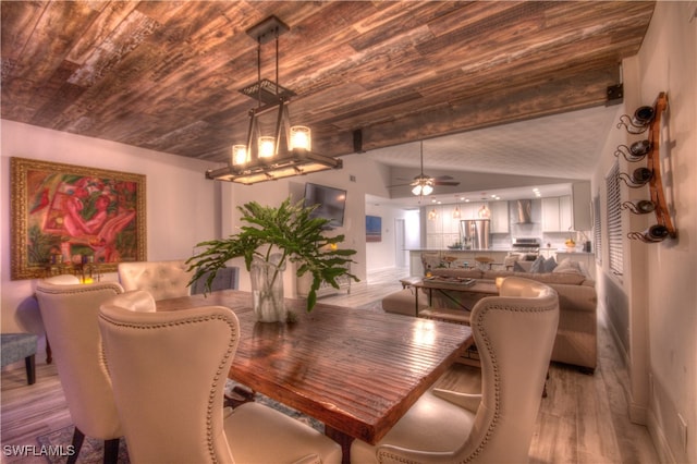 dining area with ceiling fan with notable chandelier, beamed ceiling, and light hardwood / wood-style flooring