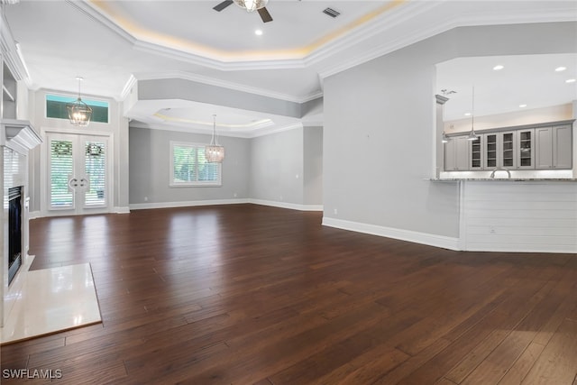 unfurnished living room featuring crown molding, a raised ceiling, ceiling fan with notable chandelier, and dark hardwood / wood-style flooring