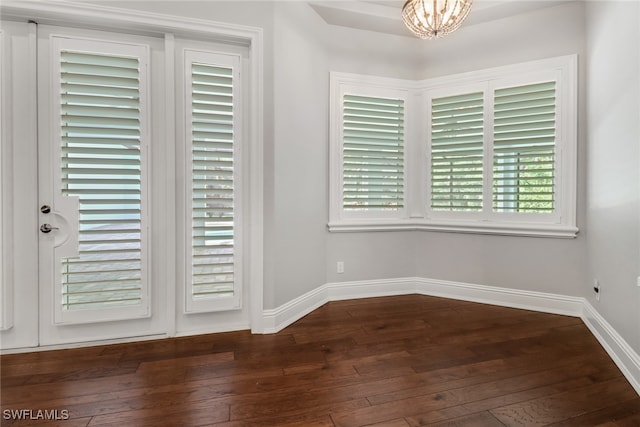 empty room with a notable chandelier, a healthy amount of sunlight, and dark hardwood / wood-style flooring