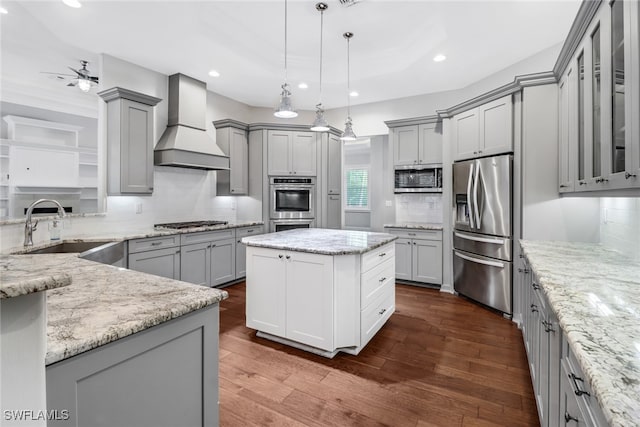 kitchen with appliances with stainless steel finishes, gray cabinets, wall chimney range hood, and a kitchen island