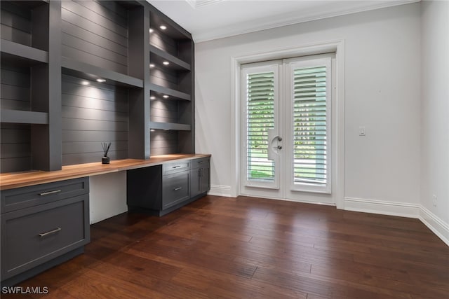 unfurnished office featuring built in desk, ornamental molding, and dark hardwood / wood-style flooring