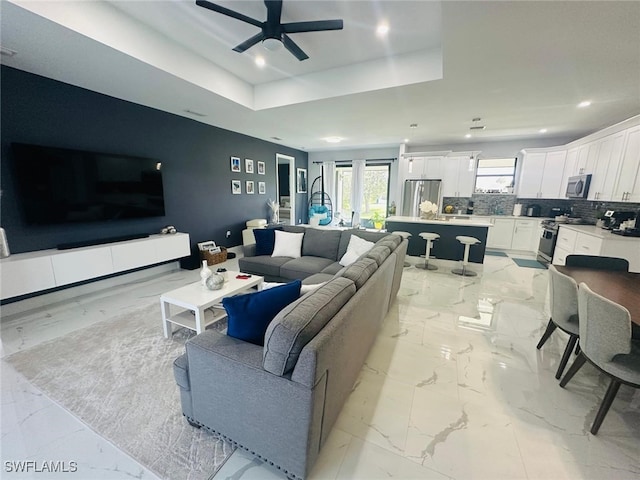 living room with a raised ceiling and ceiling fan