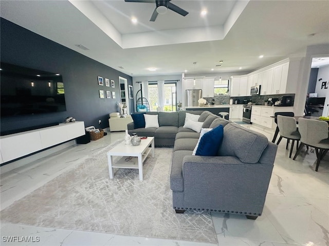 living room with a raised ceiling, french doors, and ceiling fan