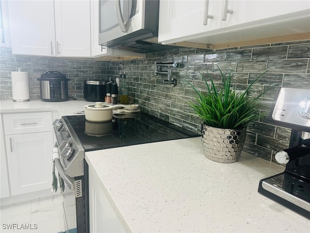 kitchen featuring light stone countertops, appliances with stainless steel finishes, white cabinets, and tasteful backsplash