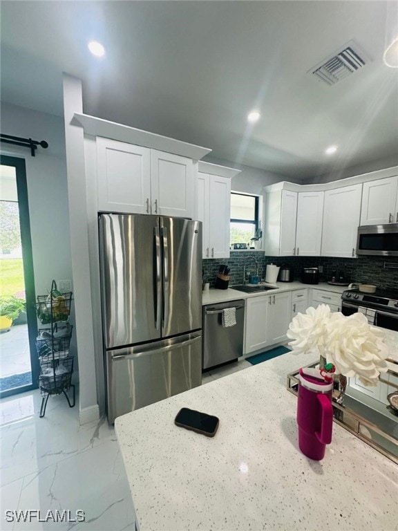 kitchen featuring white cabinets, appliances with stainless steel finishes, light stone counters, and a healthy amount of sunlight