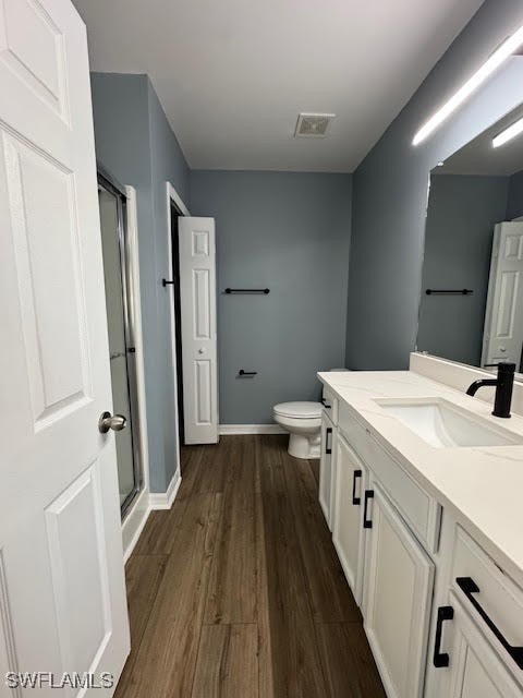 bathroom featuring a shower with door, vanity, hardwood / wood-style flooring, and toilet