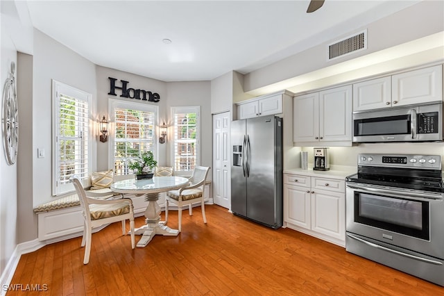 kitchen with stainless steel appliances, white cabinetry, and light hardwood / wood-style flooring