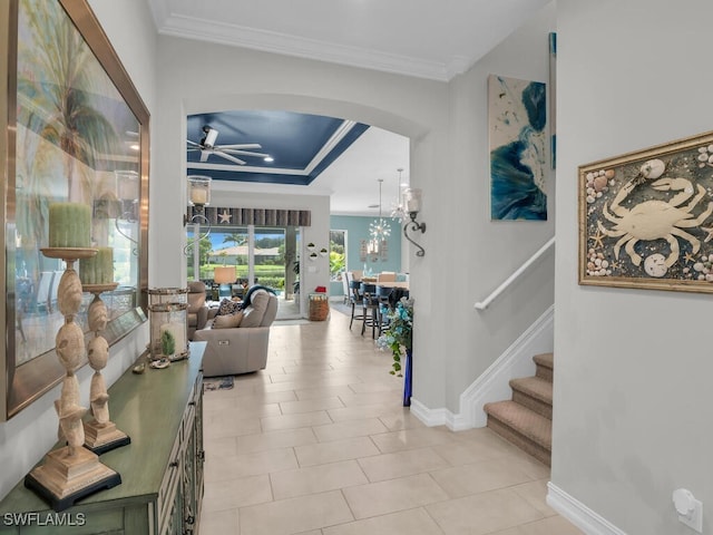 corridor featuring crown molding, light tile patterned floors, and a tray ceiling