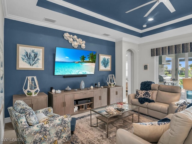 living room featuring ceiling fan, ornamental molding, and a raised ceiling