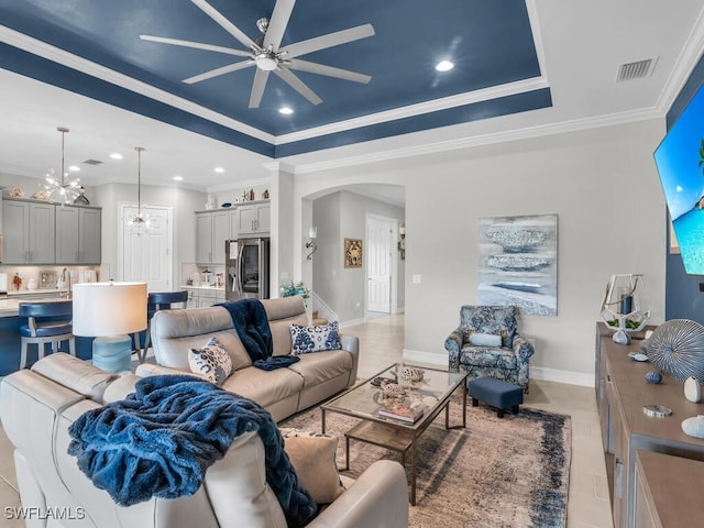 tiled living room with ceiling fan with notable chandelier, a raised ceiling, and ornamental molding