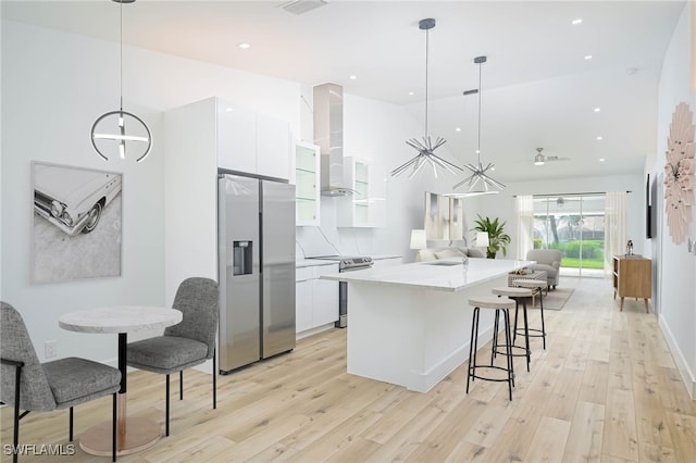 kitchen with pendant lighting, stainless steel appliances, wall chimney exhaust hood, and white cabinetry