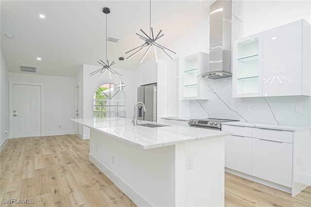 kitchen with a kitchen island with sink, wall chimney range hood, white cabinetry, and light hardwood / wood-style floors