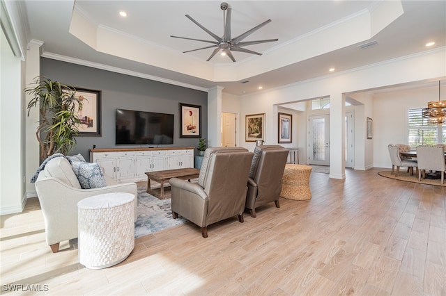 living room featuring a tray ceiling, light hardwood / wood-style floors, ceiling fan with notable chandelier, and ornamental molding