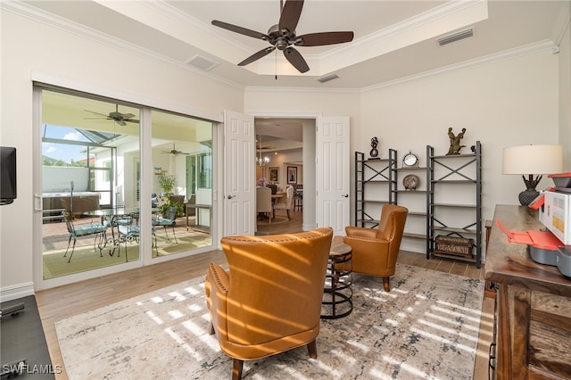 sitting room with ceiling fan, wood-type flooring, ornamental molding, and a tray ceiling