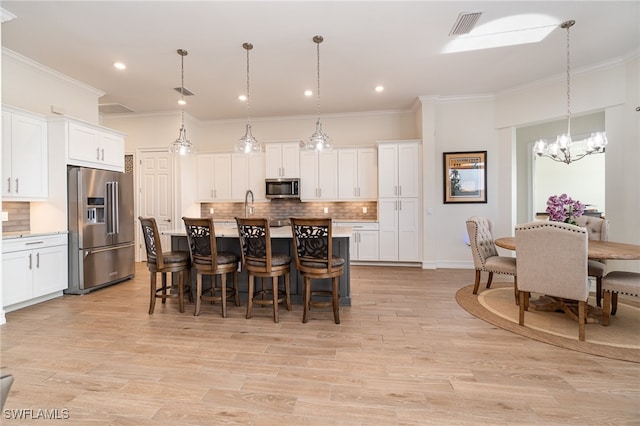 kitchen with decorative backsplash, appliances with stainless steel finishes, a center island with sink, white cabinets, and hanging light fixtures