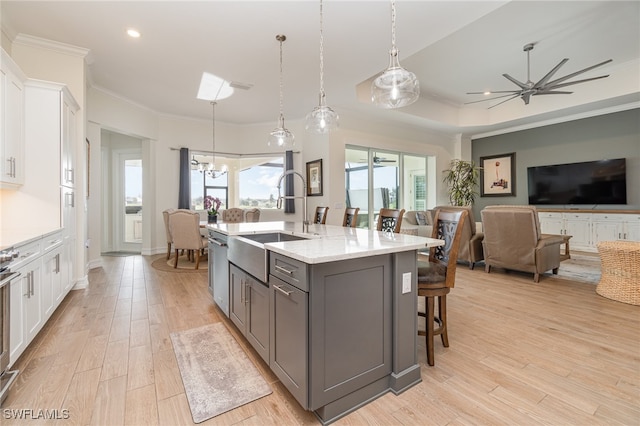 kitchen featuring light stone countertops, sink, a center island with sink, white cabinetry, and hanging light fixtures