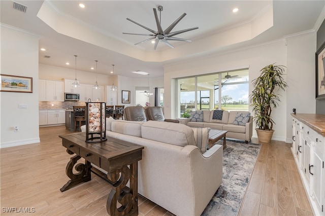 living room featuring ceiling fan with notable chandelier, a tray ceiling, light hardwood / wood-style flooring, and crown molding