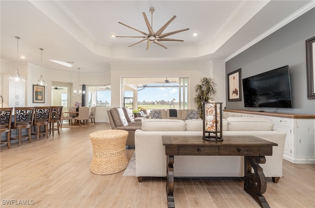 living room with light hardwood / wood-style floors, a tray ceiling, ornamental molding, and ceiling fan