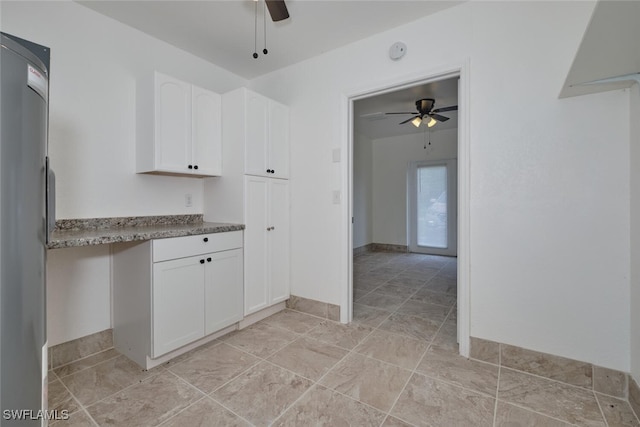 kitchen featuring ceiling fan, stainless steel refrigerator, stone counters, and white cabinetry