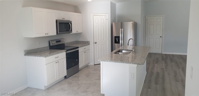 kitchen with light stone counters, an island with sink, sink, appliances with stainless steel finishes, and white cabinets