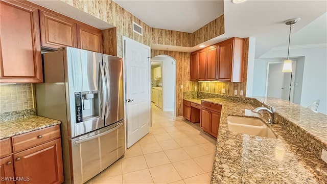 kitchen with stainless steel refrigerator with ice dispenser, sink, crown molding, light stone countertops, and decorative light fixtures