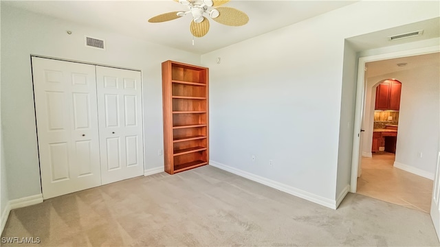 unfurnished bedroom with ceiling fan, light colored carpet, and a closet