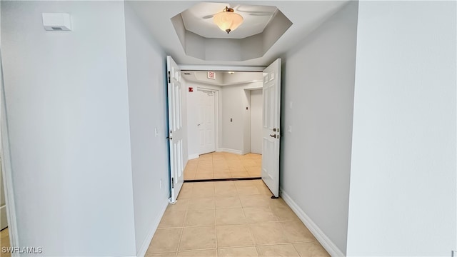 corridor featuring light tile patterned floors and a tray ceiling