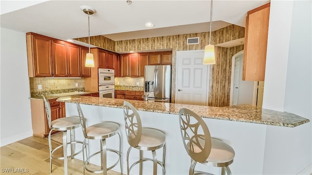 kitchen with light stone counters, light wood-type flooring, decorative light fixtures, stainless steel refrigerator with ice dispenser, and kitchen peninsula