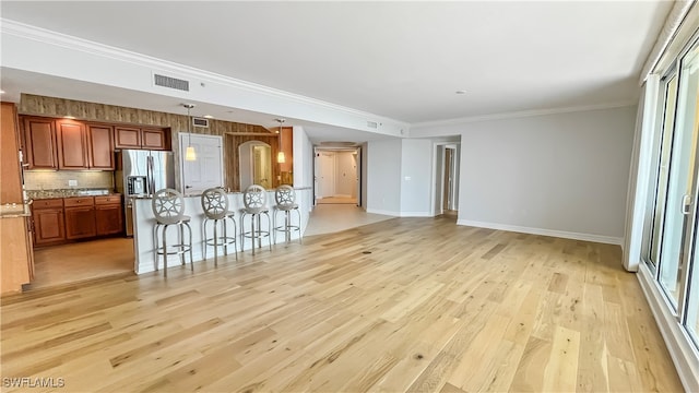 kitchen with a breakfast bar area, a center island with sink, light hardwood / wood-style flooring, and ornamental molding