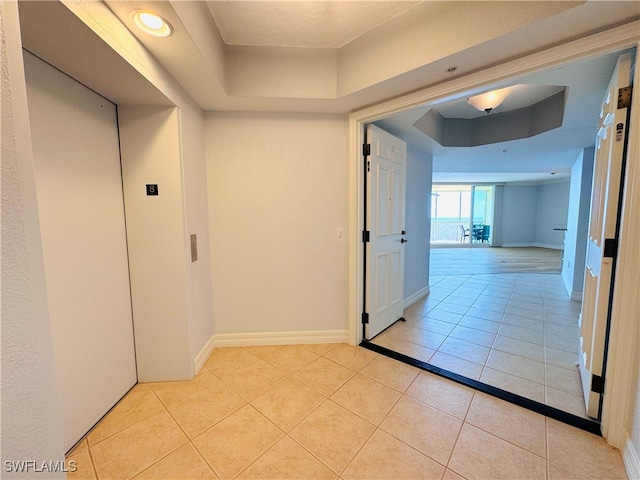 corridor with elevator, light tile patterned floors, and a raised ceiling