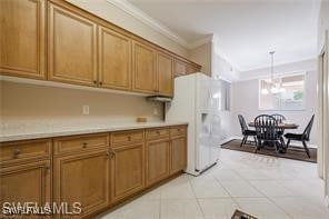 kitchen with pendant lighting, white refrigerator with ice dispenser, ornamental molding, an inviting chandelier, and light tile patterned flooring