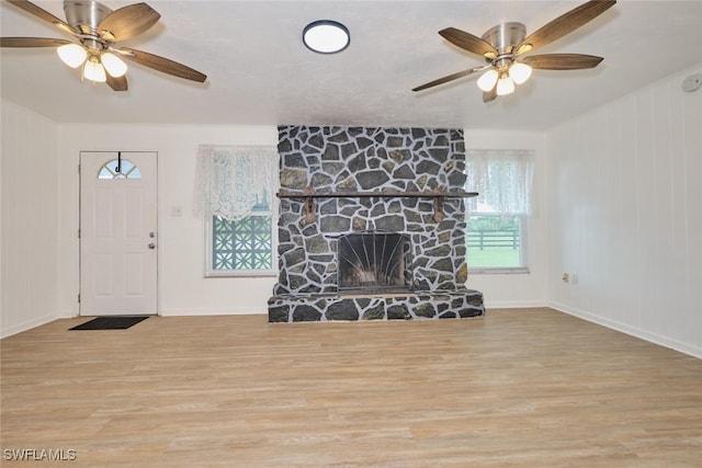 living room featuring a stone fireplace, light wood-type flooring, and ceiling fan