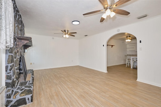 unfurnished living room featuring a stone fireplace, wooden walls, a textured ceiling, and light hardwood / wood-style flooring