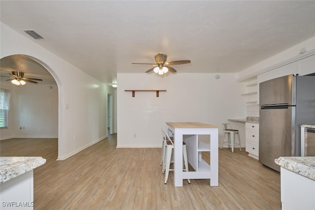 kitchen with white cabinets, stainless steel refrigerator, light wood-type flooring, and light stone counters