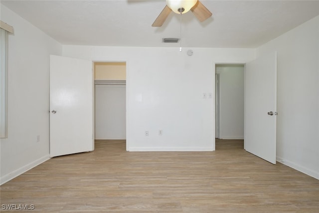 unfurnished bedroom featuring ceiling fan, a closet, light hardwood / wood-style flooring, and a walk in closet