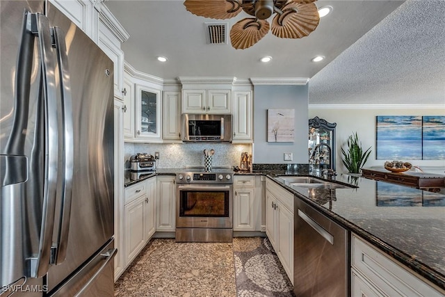 kitchen with sink, crown molding, appliances with stainless steel finishes, dark stone countertops, and white cabinets