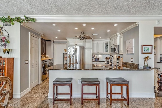 kitchen with crown molding, kitchen peninsula, stainless steel appliances, washer and clothes dryer, and white cabinets