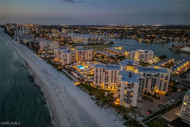 aerial view at dusk featuring a view of the beach and a water view