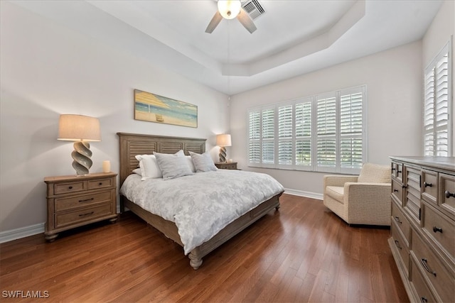 bedroom with dark wood-type flooring, a tray ceiling, and ceiling fan