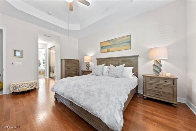 bedroom with ceiling fan, a tray ceiling, and dark hardwood / wood-style flooring