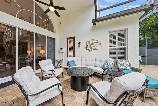 view of patio with ceiling fan, an outdoor living space with a fire pit, and glass enclosure