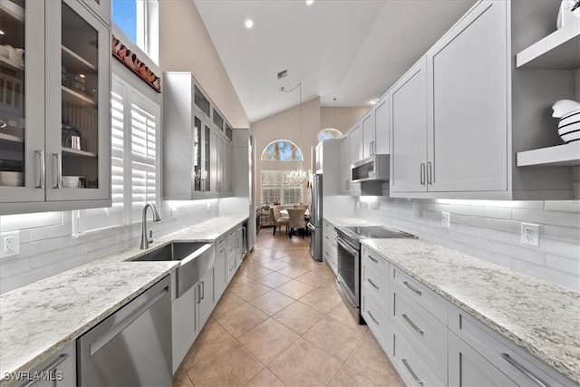 kitchen featuring pendant lighting, backsplash, appliances with stainless steel finishes, lofted ceiling, and light stone counters