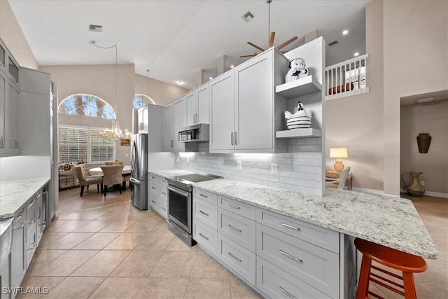 kitchen with pendant lighting, stainless steel appliances, a kitchen breakfast bar, light stone counters, and decorative backsplash