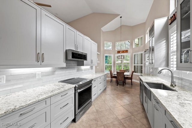 kitchen with hanging light fixtures, light tile patterned floors, appliances with stainless steel finishes, light stone counters, and ceiling fan