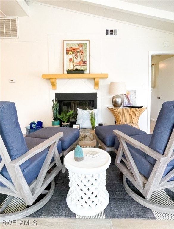 sitting room with a tile fireplace and lofted ceiling with beams